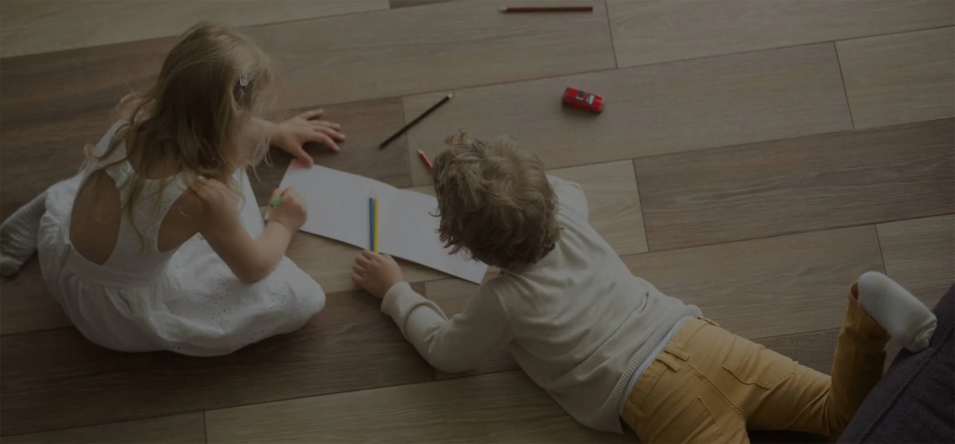 Two children coloring on laminate flooring.